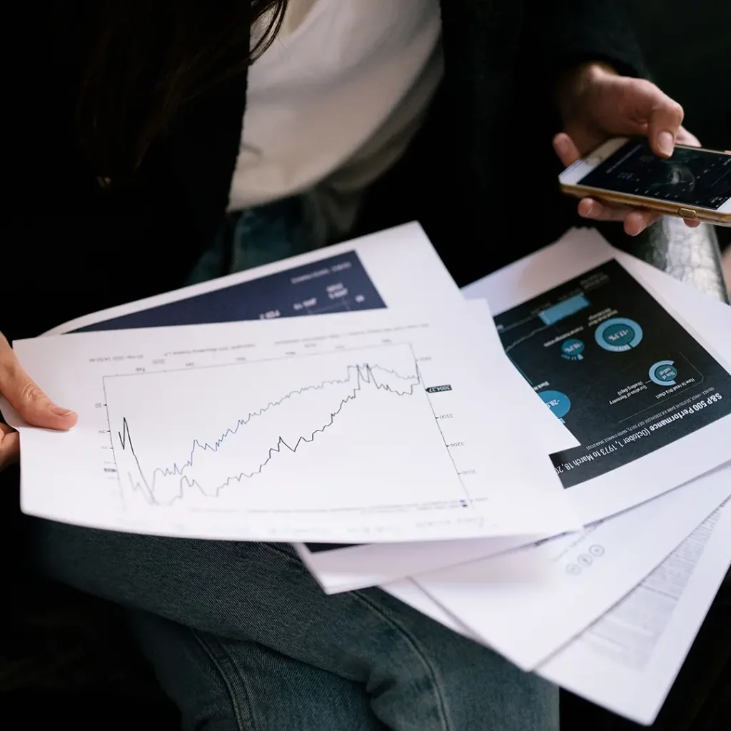 Person reviewing printed reports with line charts, data visualisations and a phone, representing business report analysis and decision-making.