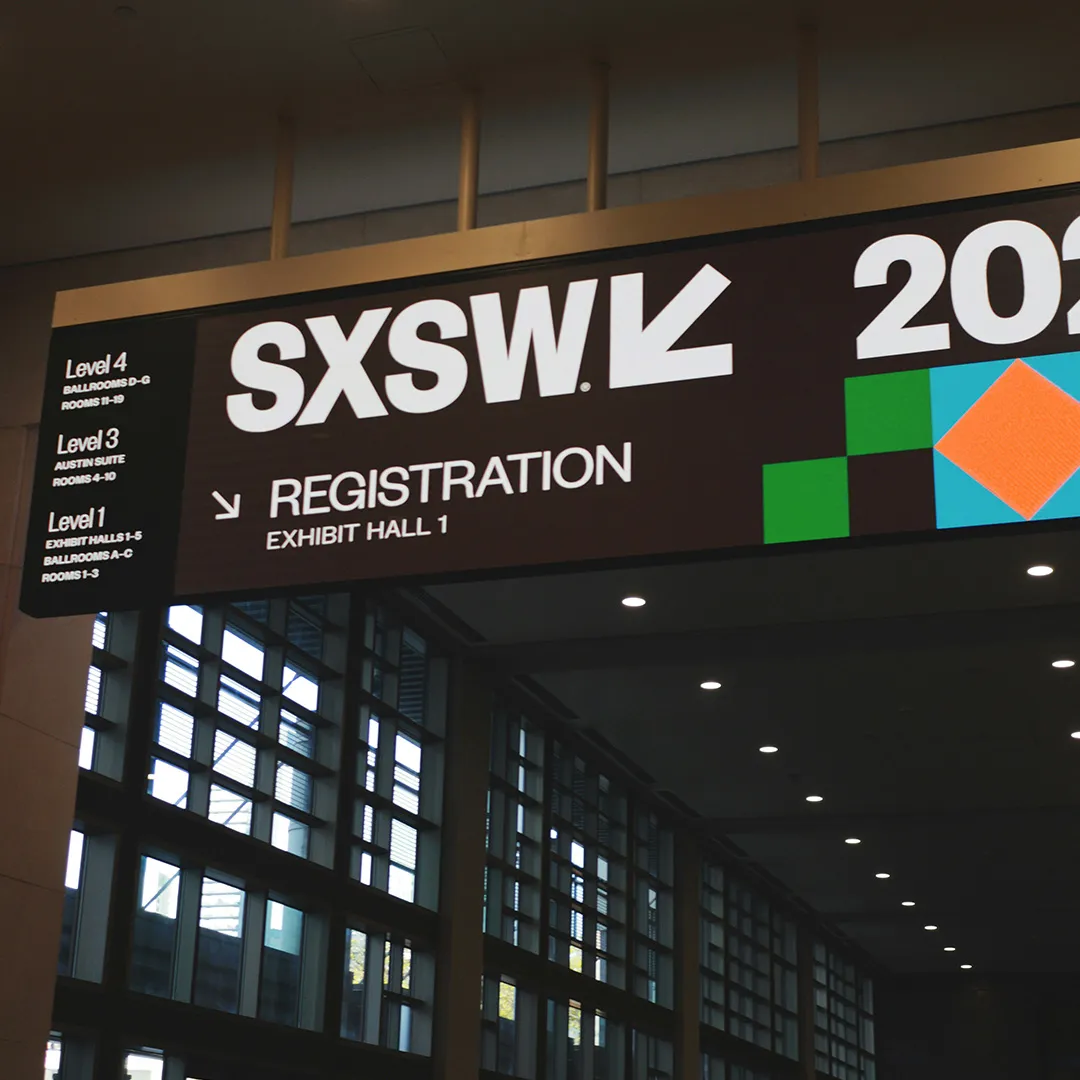 SXSW event registration signage suspended above a convention centre walkway, featuring bold branding, directional wayfinding and exhibition hall information for attendees.